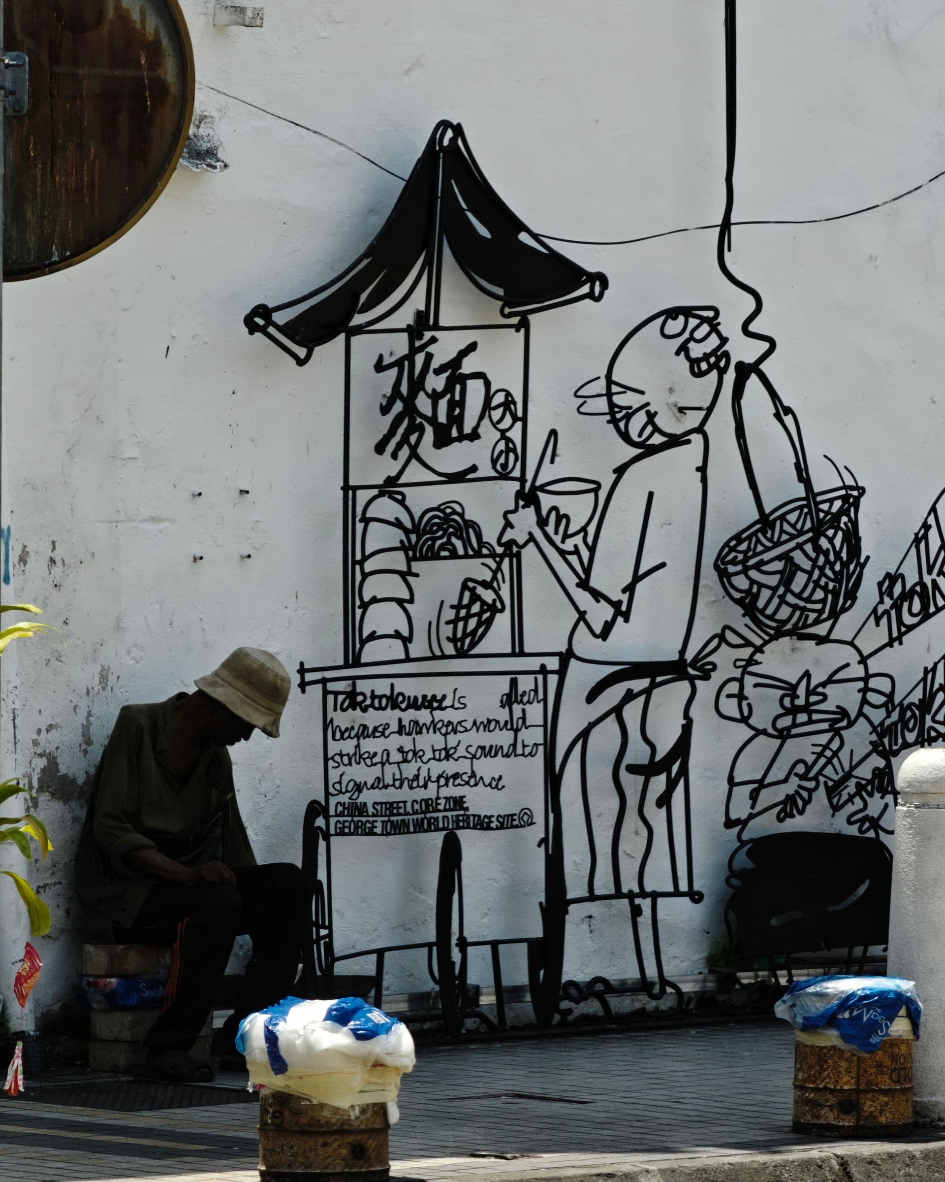 Marking George Town steel-rod sculpture of a noodle stall scene, welded wire caricature on a George Town wall