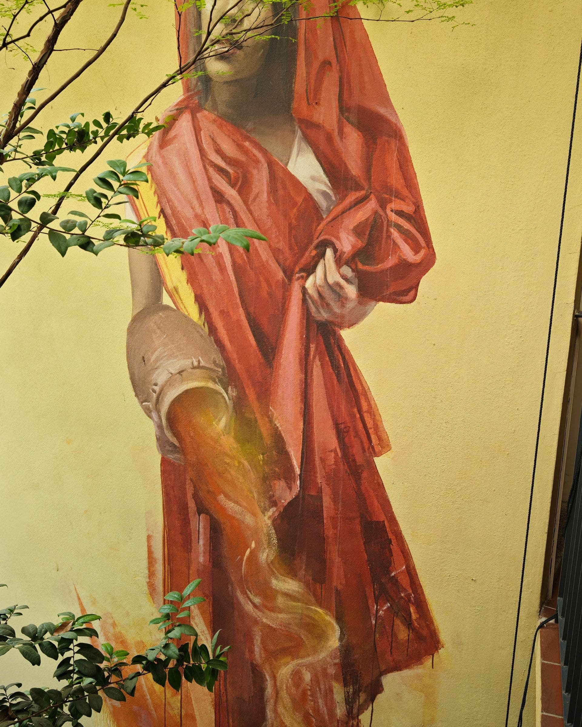 Spice Lady mural by Julia Volchkova on the Spices Hotel wall, a woman in a red dress pouring liquid from a jug